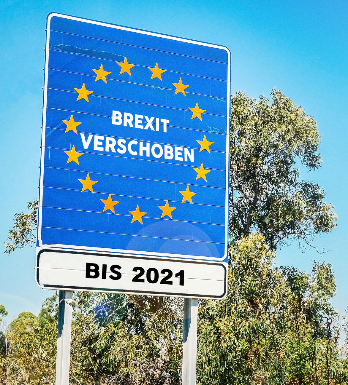 Ein großes Verkehrsschild steht vor einem blauen Himmel und Eukalyptusbäumen. Das Schild zeigt eine Reihe von zwölf gelben Sternen in kreisförmiger Anordnung gegen einen blauen Hintergrund und den Text "BREXIT VERSCHOBEN BIS 2021".