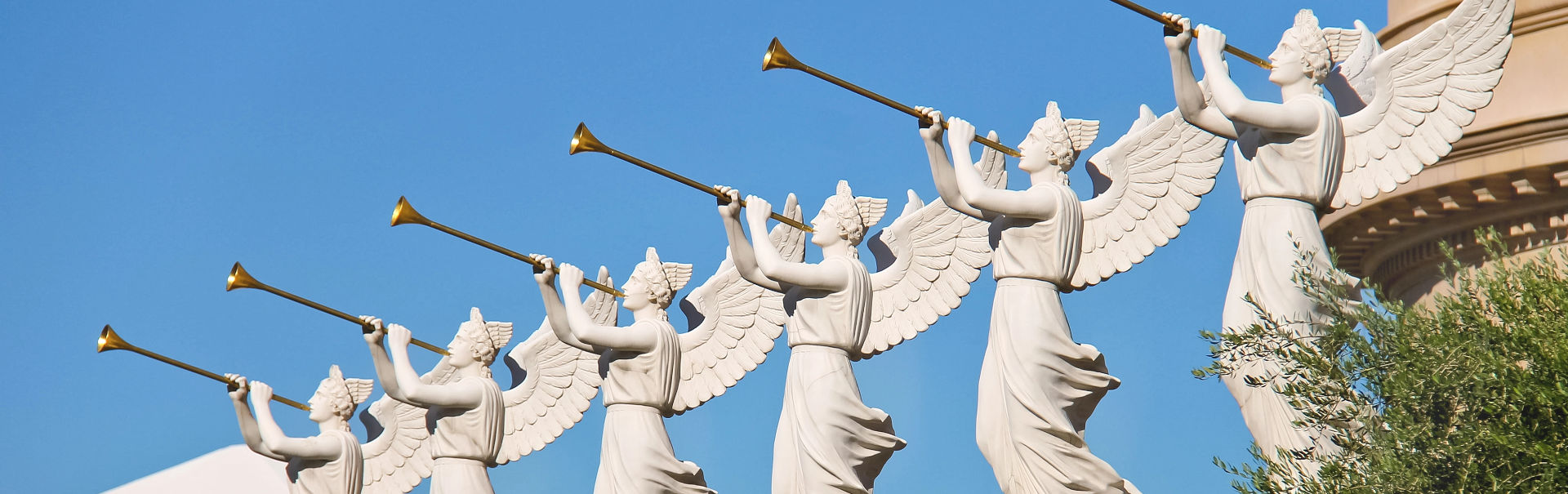 Una hilera de cinco estatuas de mensajeros celestiales, cada una representada con alas y trompetas, colocadas contra un cielo azul claro. Estas esculturas representan mensajeros que podrían compararse con los heraldos del Mazzaroth, cada uno con túnicas ondeantes y tocando sus trompetas hacia el cielo.